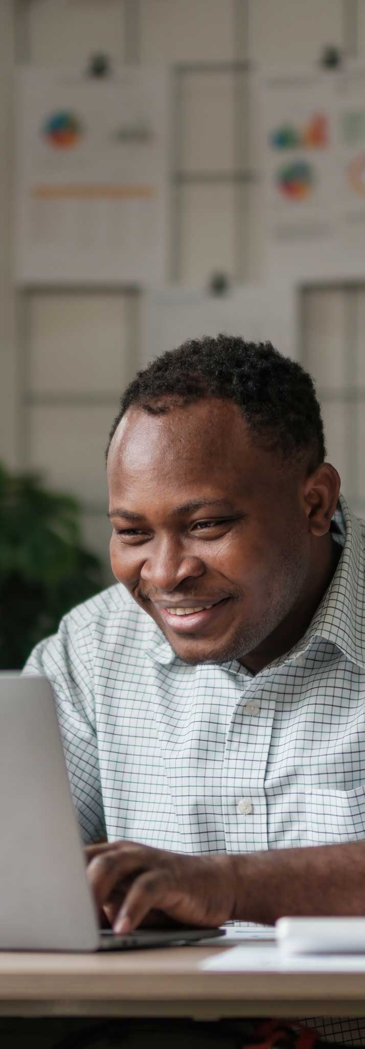 Smiling black man using laptop at home in living room. Happy mature businessman send email and working at home. African american freelancer typing on computer with paperworks and documents on table...