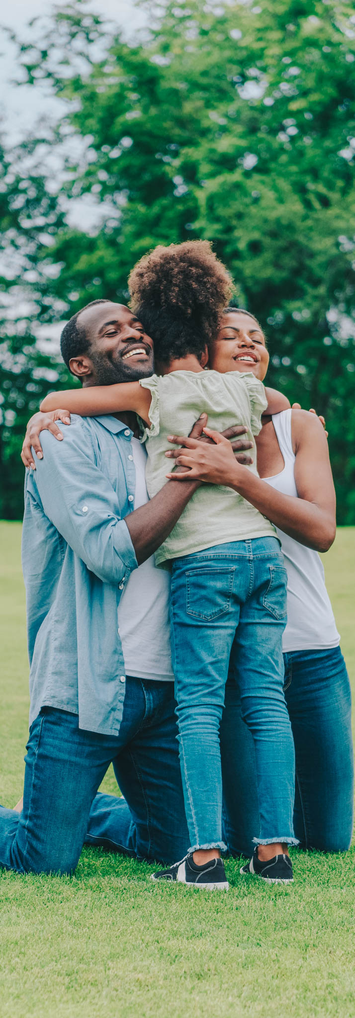 African American parents and little daughter hugging each other in park. Engedi Local foster and adoption.